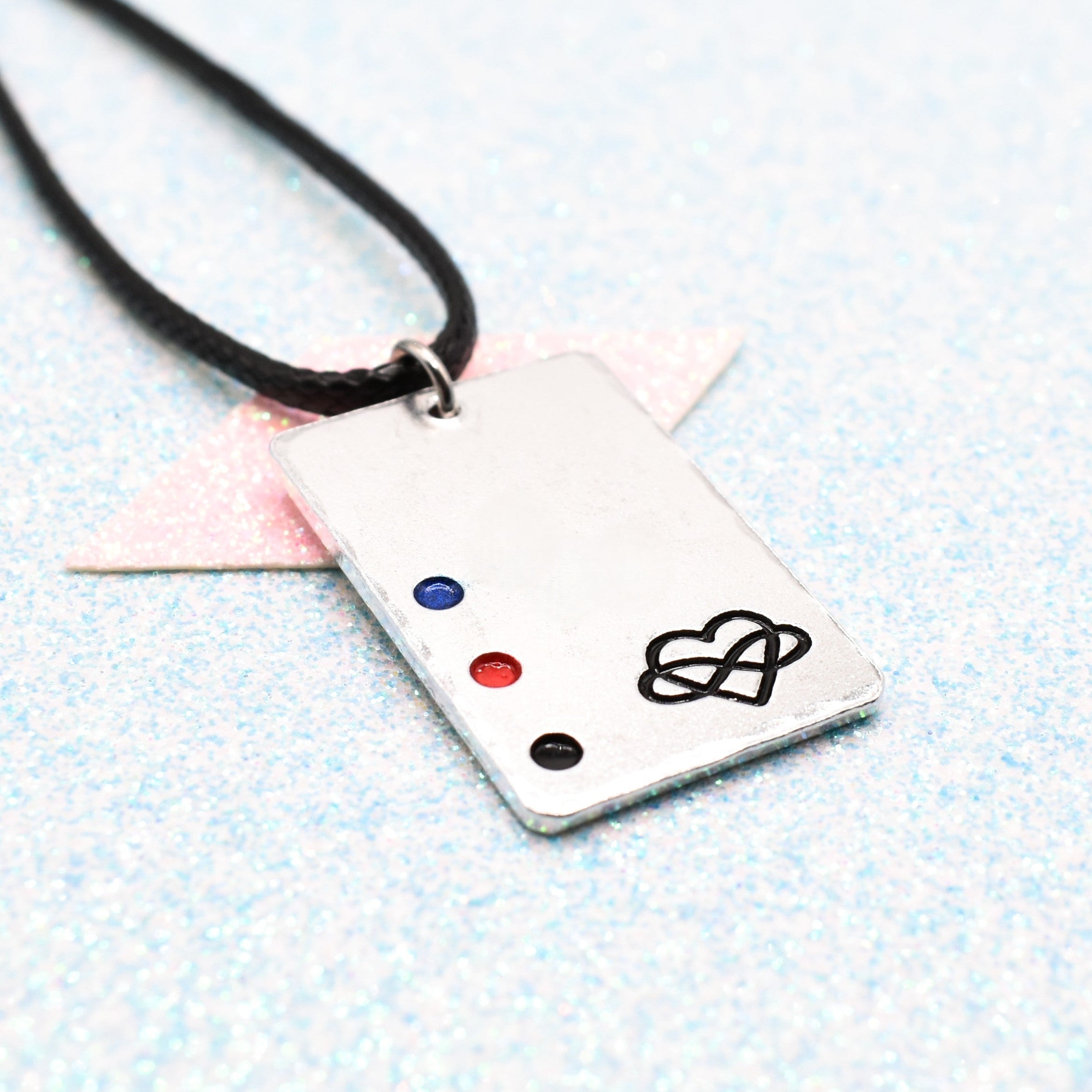 Polyamory Necklace with a rectangular tag featuring a polyamorous symbol and accents on a Leather Cord displayed on a light blue background