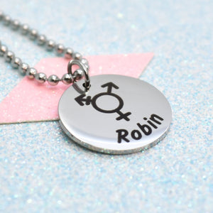 A transgender pride necklace with a silver emblem featuring a gender symbol and the name 'Robin' on it, attached to a silver chain.